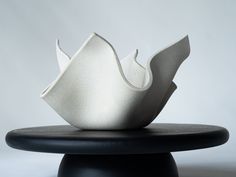 a white sculpture sitting on top of a black table next to a gray wall in the background