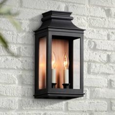 an outdoor wall light with two lit candles on the front and side, against a white brick wall