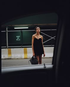 a woman in a black dress is walking down the street with her hand on her purse