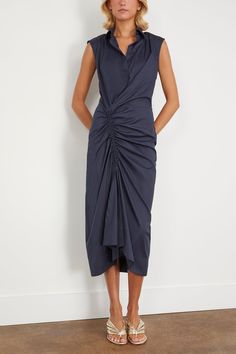 The Callas Milano Sylvie is a sleeveless shirt dress with a gathered front creating a ruched sarong design. A classic point collar and button placket front is featured at the top of the dress, while the gathering over the right leg makes a contrast to the tailored look. The dress is midi-length. Made from a light weight Italian stretch cotton poplin. FIT DESCRIPTION 69% Cotton, 25% Polyamide, 6% Elastane Sleeveless, collared, gathered dress Midi length Professional dry cleaning recommended Harri Ruched Draped Dress For Workwear, Ruched Draped Dress For Work, Ruched Sleeveless Dress For Summer Formals, Elegant Sleeveless Dress With Gathered Skirt, Midi Sleeveless Dress With Gathered Waist, Summer Formal Dress With Gathered Skirt, Ruched Sleeveless Dress For Daywear, Elegant Ruched Sleeveless Dress For Daywear, Formal Summer Dresses With Gathered Skirt