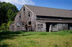 an old barn sits in the middle of a field