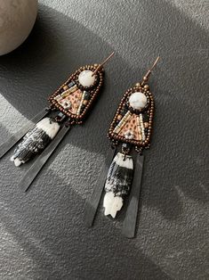 two pairs of beaded earrings with feathers and beads on top of a black surface