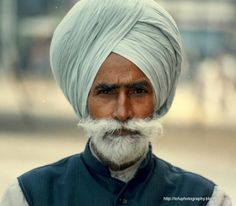 an old man with a white turban and grey beard wearing a blue vest