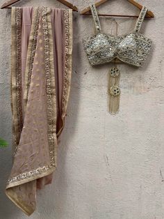 A two-piece nude gold saree set from the Priti Sahni collection. This gorgeous nude gold saree in georgette fabric is embellished with dull gold sequin, and zari border. The saree pallu is enhanced with gold butti work. The outfit is completed with a hand embroidered bustier with a mirror-sequins tassel tie-up at the back. Festive Gold Pre-draped Saree With Mirror Work, Gold Pre-draped Saree For Navratri Party, Festive Gold Pre-draped Chinon Saree, Beige Georgette Lehenga With Zari Work, Gold Anarkali-style Pre-draped Saree Embellished, Gold Embellished Anarkali Pre-draped Saree, Gold Chinon Pre-draped Saree For Navratri, Gold Embellished Pre-draped Saree, Gold Semi-stitched Designer Pre-draped Saree