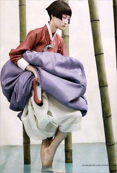 a man is standing in front of some bamboo poles and wearing a blue, purple, and white kimono