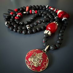 Red Ganesha Pendant Black Beaded Good Luck Necklace; Ganesha is one of the most well-known and revered Hindu deities. He is often associated with success, wisdom, and protection, making this handmade necklace an ideal talisman for anyone seeking these qualities. The black lava rock stone beads are believed to have grounding properties, helping to connect the wearer with the earth and provide a sense of stability and balance. The coral stone add a pop of color and are said to promote harmony and Hand-strung Black Jewelry For Festivals, Handmade Amulet Mala For Rituals, Handmade Mala Amulet For Rituals, Traditional Red Necklace With Black Beads, Handmade Red Temple Necklace For Festivals, Traditional Red Necklaces With Black Beads, Handmade Red Temple Necklace, Black Amulet Necklaces With Polished Beads, Black Amulet Necklace With Polished Beads