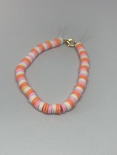 an orange, pink and white necklace with gold clasp on a gray background is shown