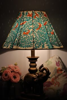 an elephant lamp sitting on top of a table next to a flowered vase and pillow