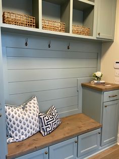 a wooden bench with two pillows on it in a room that has blue cabinets and white walls