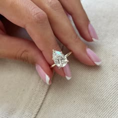 a woman's hand with pink and white manicured nails holding a diamond ring