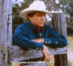 a man wearing a cowboy hat leaning on a wooden fence with his arms crossed and looking at the camera