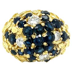 One 18 karat yellow gold (stamped 18K) carved flower design dome ring set with four (4) modern round brilliant cut diamonds, approximately 0.70 carat total weight with matching I/J color and SI1 clarity and twenty-six (26) round natural dark blue sapphires, approximately 2.00 carat total weight. The ring is a finger size 6.25 and can be resized. Sizing is not included. Dome Ring, Domed Ring, Diamond Flower, Modern Round, Gold Flower, Gold Flowers, Sapphire Diamond, Round Brilliant Cut Diamond, Round Brilliant Cut