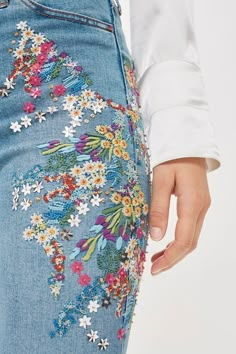 a woman in white shirt and jeans with flowers on the bottom half of her pants