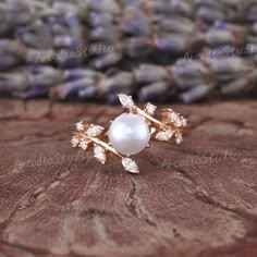 a pearl and diamond ring sitting on top of a piece of wood with lavender flowers in the background