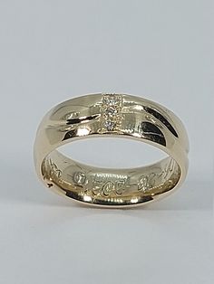 a yellow gold wedding ring with an inscription on the side and a diamond in the center