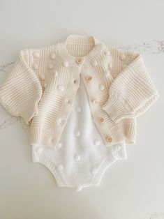 Soft and cozy, this stunning knit cardigan is the perfect addition to your little ones closet. Tiny Pom Pom appliqués all over. Textured pattern with front buttons. Playful Knit Long Sleeve Outerwear, Cute Cotton Cable Knit Sweater, Cute Cream Soft Knit Sweater, Cute Cream Cotton Cardigan, Playful Cotton Knitted Cardigan, Cute Knitted Cotton Cardigan, Playful Knitted Cotton Cardigan, Playful Cream Winter Sweater, Playful Winter Cardigan