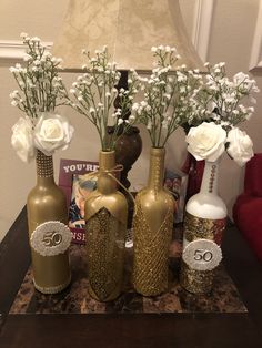 three vases with flowers in them sitting on a table next to a lamp and pictures