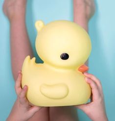 a person holding a yellow rubber ducky in front of their face and legs,