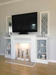 a flat screen tv mounted on the wall above a fireplace with candles in front of it