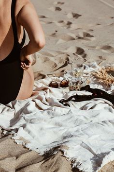 a woman sitting on top of a sandy beach next to a bottle of wine and straw