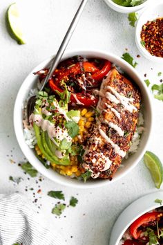 two bowls filled with meat and vegetables on top of a white table next to lime wedges