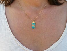 a woman wearing a gold necklace with two blue squares on the front and one yellow square on the back