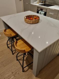 a kitchen island with two stools and a basket of fruit on it's counter