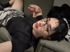 a young man laying on top of a couch next to a black shirt and glasses