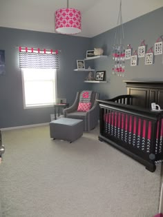 a baby's room with gray walls, pink and white decor, and a black crib