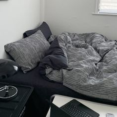 an unmade bed sitting next to a table with a keyboard on top of it