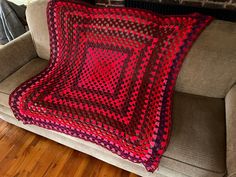 a red and black crocheted afghan sitting on a couch next to a brick wall