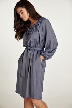 This belted dress is crafted in blue denim style woven viscose fabric. It has a wide round neckline with an internal tie allowing either for ruching or an off-shoulder look. The tie is in the same fabric with metal stoppers at the ends. There is a V opening below the neckline. It has long raglan sleeves with elastic at the cuffs creating gathers. There is an inseam pocket on either side. The dress can be worn without the belt for a sack silhouette. The belt is included. Gentle machine wash. Turn garment inside out. Cold water. Mild detergent. Iron on reverse side. Do not tumble dry. Do not bleach. Chic Blue Dress With Belted Cuffs, Blue Midi Dress With Belted Cuffs, Elegant Denim Daywear Dress, Elegant Belted Denim Dress, Elegant Denim Dress For Daywear, Casual Blue Dresses With Tie Fastening, Casual Blue Dress With Tie Fastening, Denim Blue Midi Dress For Brunch, Blue Tie Fastening Dress For Daywear