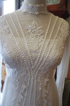 a white wedding dress on display in a room with a mannequin behind it