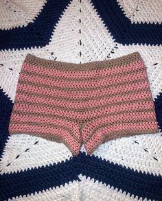 a crocheted blanket that is laying on top of a bed with pink and brown shorts