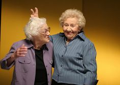 two older women standing next to each other with their hands in the air and smiling