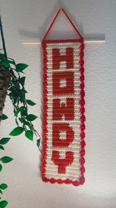 a crocheted sign hanging on the wall next to a potted green plant