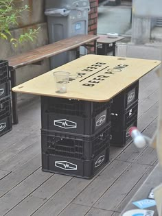 three crates sitting on top of a wooden floor next to a bench and table with drinks in it