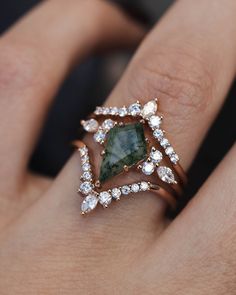 a woman's hand with a diamond and green stone ring on top of it