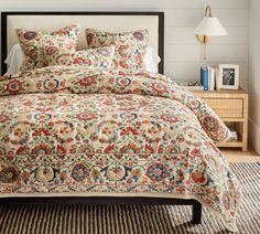 a bedroom with a bed covered in a multicolored comforter and matching pillows