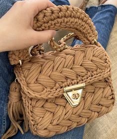 a person holding a brown woven purse in their hand and sitting on a couch with her legs crossed