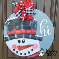 a door hanger with a snowman painted on it's face and red bow