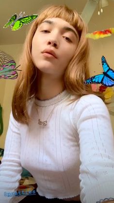 a woman with long hair wearing a white sweater and butterfly necklace