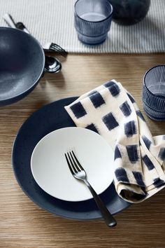 an empty plate with a fork and knife on it next to other plates, cups and utensils