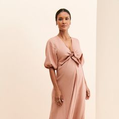 a pregnant woman in a pink dress poses for the camera with her hands on her hips