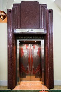 an elevator with red and silver doors in a large room that has green carpeting on the floor