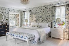 a bedroom decorated in blue and white with floral wallpaper, a large bed, two nightstands, and a chandelier