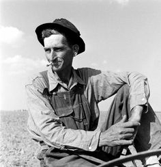 black and white photograph of a man sitting on a boat in the water wearing a hat