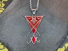 Embrace the enigmatic allure of the Sigil of Lucifer Pendant Necklace, adorned with striking red enamel and gleaming gemstone accents. Crafted from durable stainless steel, this necklace encapsulates the essence of the Seal of Satan. At its heart lies the potent Sigil of Lucifer, symbolizing enlightenment, defiance, and the pursuit of higher knowledge. Encircled by a mesmerizing pentagram, this pendant exudes an aura of mystique and power. Each pendant is meticulously crafted, with attention to Lucifer Ring, Red Gothic Metal Necklace, Satanic Jewelry, Necklaces Satanic, Silver Pentagram Necklace, Inverted Pentagram, Gemstone Necklace Pendant, Gemstone Pendant, Silver Color