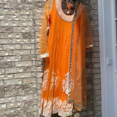 Gorgeous Orange With White Embroidery Net Material With White Design And Cream Gold Border Top Is Lined Churidar Dry Clean Only Never Worn Approximate Measurements Laying Flat Length - 48-49” Pit To Pit - 21” Full Sleeves Are Ruched Are The Arms Designer Orange Salwar Kameez, Orange Kurta With Cutdana For Eid, Orange Cutdana Kurta For Eid, Orange Kurta With Sheer Dupatta For Navratri, Orange Salwar Kameez With Cutdana For Navratri, Semi-stitched Orange Cutdana Anarkali Set, Orange Chanderi Anarkali Set With Cutdana, Designer Orange Sharara With Sheer Dupatta, Orange Anarkali Set With Dupatta