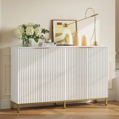 a white sideboard sitting on top of a wooden floor next to a vase with flowers